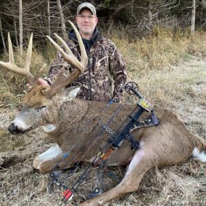 A man in camouflage sitting next to a large deer.